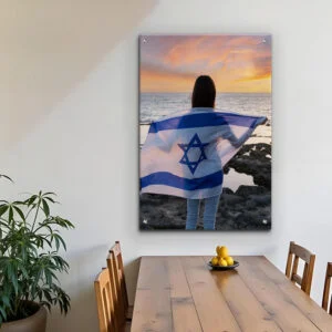 תמונת זכוכית אמנותית של בחורה עם דגל ישראל בשקיעה, עם שמיים צבעוניים וים שקט ברקע.