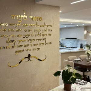 מזמור לתודה באותיות פרספקס בצבע זהב מרחפות על קיר שיש בבית יוקרתי, עם פינת אוכל מודרנית ברקע.